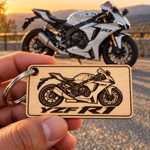 May include: A rectangular wooden keychain featuring a laser-engraved illustration of a sport motorcycle. The design includes the text YZF-R1 positioned below the motorcycle graphic. A silver metal split ring is attached to the top left corner.