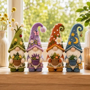 May include: Four crocheted gnome figurines standing in a row. Each gnome wears a tall, pointed hat decorated with floral, butterfly, or celestial motifs and holds a small crocheted pot containing flowers. The gnomes feature white yarn beards.