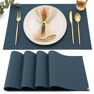Puede incluir: Un juego de manteles individuales rectangulares de color azul oscuro con textura tejida. Se muestra un mantel con un plato blanco, una servilleta beige sujeta por un anillo dorado, tenedor, cuchillo, cuchara dorados y un vaso con líquido ámbar.