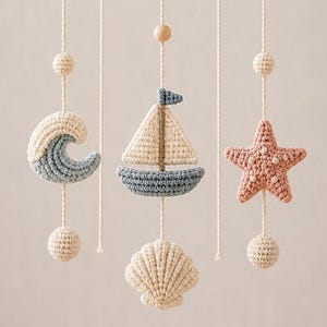 May include: A hanging mobile featuring a circular wooden frame with cream-colored cords suspending crocheted nautical elements including a blue wave, a sailboat with a cream sail and blue hull, a pink starfish, and a cream-colored seashell.