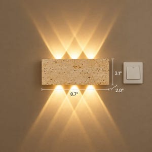May include: A rectangular beige stone wall lamp with a porous texture, emitting warm light beams upward and downward. The fixture measures 8.7 inches in width, 3.1 inches in height, and 2.0 inches in depth, positioned next to a white light switch.