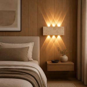 May include: A rectangular wall-mounted light fixture with a textured beige stone finish. The lamp emits warm, bright light in six distinct beams, three directed upward and three directed downward, creating a symmetrical pattern on the wooden wall.
