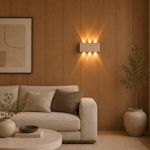 May include: A rectangular wall sconce with a speckled stone-like finish mounted on a wood-paneled wall. The fixture emits light in six distinct beams, three directed upward and three directed downward, creating a bright, warm glow on the surface.