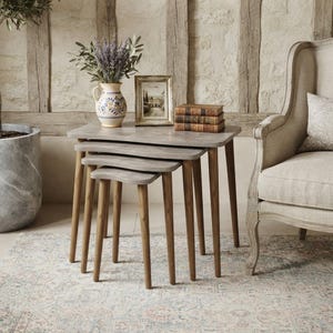 May include: A set of three nesting tables with light grey rectangular tops and four tapered wooden legs each. The tables are stacked together, featuring a smooth finish and a clean design that allows them to fit neatly underneath one another.