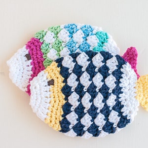 May include: Two crocheted fish ornaments in a variety of colors, including pink, green, blue, yellow, white, and navy blue. The fish are stacked on top of each other.