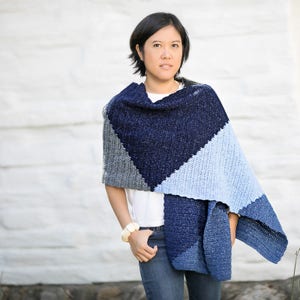 May include: A blue, gray, and light blue shawl with a geometric design. The shawl is draped over the shoulders and arms. The shawl is made of a soft, textured material.