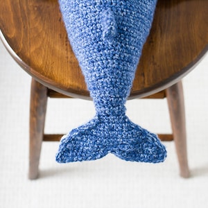 May include: A blue crocheted dolphin tail with a white background.
