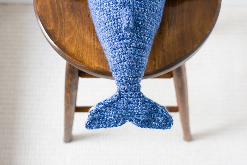 May include: A blue crocheted dolphin tail with a white background.