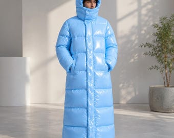 May include: A long, light blue puffer coat with a glossy, reflective finish. The coat features a high-neck hood, long sleeves, and a full-length front closure with visible snap buttons. The quilted design consists of horizontal baffles throughout.