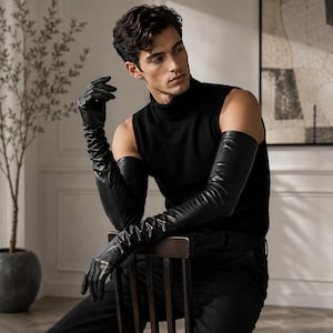 Puede incluir: Un par de guantes de cuero negro de longitud ópera que se extienden más allá de los codos, con una textura suave y ajustada. Los guantes se llevan con una camiseta negra sin mangas de cuello alto y pantalones negros, creando un conjunto monocromático.