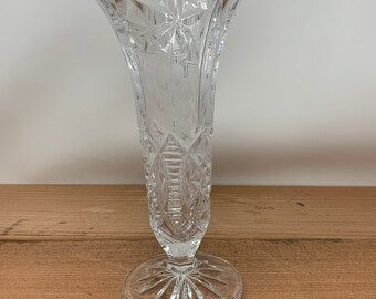 May include: A clear glass vase with a cut glass design. The vase has a flared top and a round base.