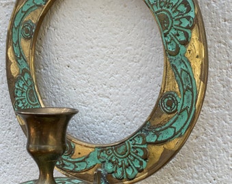 May include: A gold-toned wall-mounted candle holder with a decorative green floral design. The holder has a circular base and a single candle cup.