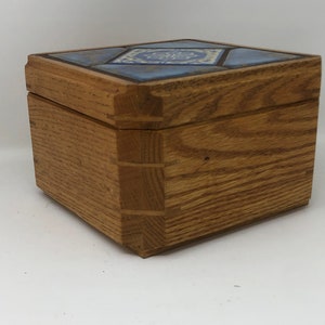 May include: A wooden box with a blue and white tile top. The box is made of light brown wood and has a simple design.