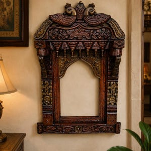 May include: A rectangular wooden wall frame featuring intricate hand-carved details, including two bird figures at the top, floral motifs, and a central arched opening. The wood has a dark brown finish with gold-toned accents on the carvings.