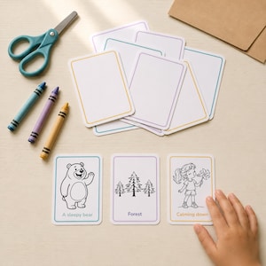 Overhead photo of three printable story prompt cards on a table - A Sleepy Bear, Forest, and Calming Down - with a child's hand reaching for one, surrounded by crayons, scissors, and a kraft envelope, from the AiWhizzkids 36 Story Prompt Cards printable deck.