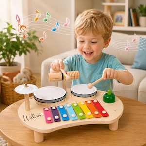 May include: A wooden musical toy set featuring a xylophone with colorful metal keys, two white drums, a small cymbal, a green bell, and a wooden guiro. The light-colored wooden base is personalized with the name William in black script.