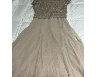Peut inclure: Une robe longue au sol avec un corsage beige doté d'une superposition de dentelle texturée en forme d'écailles et de manches courtes. La jupe est composée d'un tissu beige clair fluide et transparent qui tombe de la taille jusqu'à l'ourlet.