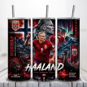 May include: A cylindrical metal tumbler with a straw featuring a graphic print of a soccer player in a red jersey, the Norwegian flag, a Viking ship, and text including "NORWAY," "HAALAND," "VIKING, WARRIOR, LEGEND," and "2026 FIFA WORLD CUP."