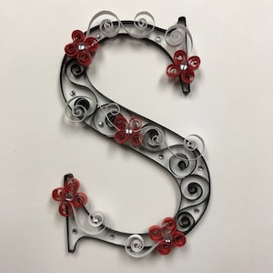 Può includere: Una lettera S in carta quilling decorata con fiori rossi e spirali bianche e nere.