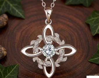 May include: A silver-toned pendant necklace featuring a central round clear gemstone surrounded by a four-pointed knot design with leaf-like detailing. The pendant hangs from a delicate silver chain and includes the text Virella London.