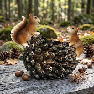 May include: A decorative planter shaped like a large brown pinecone with two small brown squirrels attached to the sides. One squirrel is perched on the top edge with a bushy tail, while the other stands on the opposite side, both facing inward.
