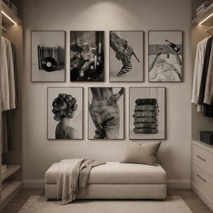 May include: A gallery wall featuring seven black and white framed prints displayed above a beige upholstered bench. The artwork depicts various lifestyle scenes including vinyl records, a champagne toast, high heels, and folded denim jeans.