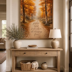 May include: A rectangular framed wall art print featuring an autumn forest path with the text 'praise God from whom all blessings flow' centered on the trail. The artwork displays orange and yellow trees under a soft, hazy light.