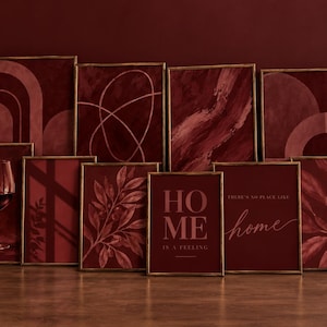 May include: A collection of ten rectangular wall art prints in thin gold frames, featuring deep burgundy and maroon tones. Designs include abstract geometric shapes, botanical leaf patterns, a wine glass, and text reading HOME IS A FEELING.