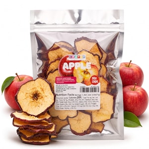 Op de afbeelding: Een doorzichtige plastic zak gevuld met gedroogde appelschijfjes, gelabeld als Crafty Confections Apple Dry Chips. De verpakking bevat voedingswaarden en een nettogewicht van 71g. Twee hele rode appels met groene blaadjes liggen naast de zak.