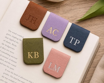 Pode incluir: Cinco marcadores de página magnéticos retangulares nas cores castanho, lavanda, azul-marinho, verde-azeitona e rosa seco. Cada marcador apresenta duas letras maiúsculas em relevo: JH, AC, TP, KB e LM. Estão dispostos nas páginas de um livro.
