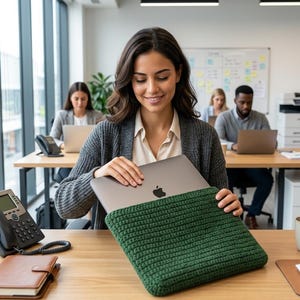 May include: A dark green, rectangular, crocheted laptop sleeve with a textured, ribbed stitch pattern. The sleeve is designed to hold a thin, silver laptop with a visible Apple logo on the lid, providing a protective cover for the device.