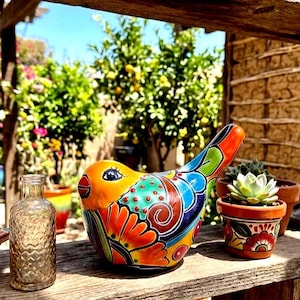 May include: A colorful ceramic bird figurine with orange, green, blue, and red floral patterns sits on a wooden shelf next to a small clear glass bottle, a succulent in a painted terracotta pot, and a stack of decorative square tiles.