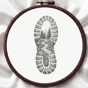 May include: A circular wooden embroidery hoop containing white fabric with a cross-stitch design of a boot tread. Inside the tread pattern is a detailed landscape featuring a winding path, evergreen trees, and small flowers in shades of gray.