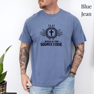 May include: A blue jean colored short-sleeve t-shirt featuring a black graphic of a computer circuit board with a cross in the center. Below the graphic, the text reads "JESUS IS THE SOURCE CODE" in a bold, black, sans-serif font.