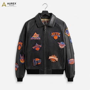 May include: A black leather bomber jacket featuring a collared neckline, a front zipper closure, and ribbed cuffs and hem. The jacket is decorated with various embroidered patches, including basketball-themed designs and the text KITH and KNICKS.