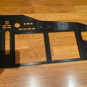 Puede incluir: Un marco de panel de instrumentos de avión impreso en 3D de color negro, con múltiples recortes rectangulares para pantallas, aberturas circulares para indicadores y varias ranuras rectangulares pequeñas para interruptores, todo dispuesto en una configuración plana y modular.