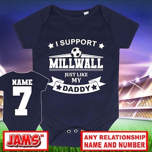 Peut inclure: Un body pour bébé bleu marine avec le texte blanc I SUPPORT MILLWALL JUST LIKE MY DADDY et un ballon de football. Une vue plus petite montre le dos du body avec le mot NAME et le chiffre 7 imprimés en blanc sur le tissu.