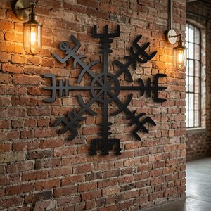 Könnte beinhalten: Ein schwarzes Vegvisir-Wandkunstobjekt aus Metall mit einer zentralen kreisförmigen Nabe und acht strahlenförmigen Armen, die jeweils in unterschiedlichen, komplexen geometrischen Symbolen enden. Das Design ist symmetrisch und matt.