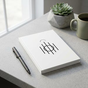 May include: A white notebook with a black graphic design consisting of a central circle intersected by five vertical lines and a small arc above. A black ballpoint pen lies next to the notebook, accompanied by a green succulent and a mug.