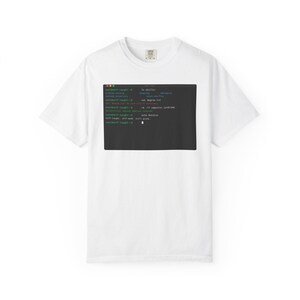 May include: A white short-sleeved t-shirt featuring a central graphic of a dark gray computer terminal window. The terminal displays command-line text in green, white, and blue, including the phrases user@self-taught, cat degree.txt, and self-taught, self-made, still going.
