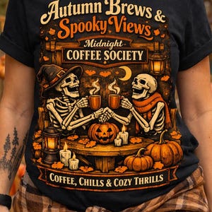 Peut inclure: Un t-shirt noir avec une impression graphique portant le texte "Autumn Brews & Spooky Views", "Midnight COFFEE SOCIETY" et "COFFEE, CHILLS & COZY THRILLS". Le motif montre deux squelettes buvant du café à une table avec des citrouilles.