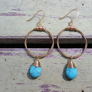 May include: A pair of gold hoop earrings with turquoise stone drops. The hoops are made of wire and the stones are wrapped in wire.