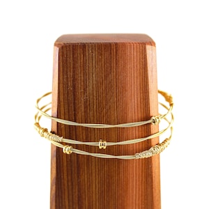 May include: A gold bracelet made from three strands of wire with small gold beads. The bracelet is displayed on a wooden stand.