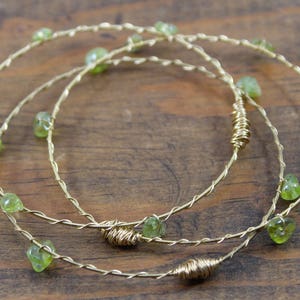 May include: Three gold wire bracelets with green gemstone accents. The bracelets are intertwined and feature a twisted wire design.