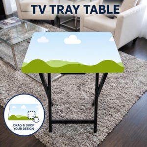 May include: A rectangular TV tray table with black metal legs and a flat top surface featuring a printed graphic of green rolling hills under a light blue sky with white clouds. The text TV TRAY TABLE is visible at the top of the image.