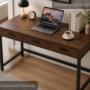 Könnte beinhalten: Ein rechteckiger Schreibtisch mit dunkler Holzmaserung und drei Schubladen mit schwarzen Metallgriffen. Der Schreibtisch wird von einem schwarzen Metallrahmen getragen. Auf der Oberfläche stehen ein Laptop, eine Uhr, eine Lampe und Bücher.