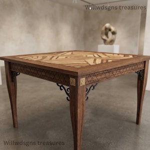 Pode incluir: Uma mesa quadrada de madeira com um padrão geométrico de parquet no tampo, pernas de madeira escura e detalhes esculpidos ao longo da saia. A mesa inclui suportes de canto de metal preto e pequenos detalhes em latão. O texto Willwdsgns treasures é visível.