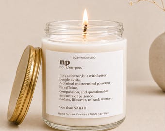 May include: A clear glass jar candle with a lit wick and a gold-colored metal lid resting beside it. The white label reads: COZY WAX STUDIO np noun/en-pee/ Like a doctor, but with better people skills. A clinical mastermind powered by caffeine, compassion, and questionable amounts of patience. badass, lifesaver, miracle worker See also: SARAH Hand Poured Candles | 100% Soy Wax
