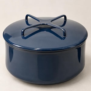 May include: A deep navy blue circular ceramic storage container with a matching lid. The lid features a distinctive raised cross-shaped handle made of the same glossy navy blue material, providing a secure grip for lifting the lid off the base.