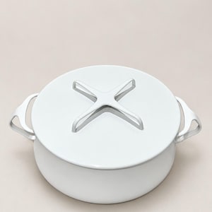 May include: A round, white cooking pot with a smooth finish and two side handles. The lid features a distinctive, raised cross-shaped handle centered on top. The entire piece is monochromatic, showcasing a clean, minimalist design with curved edges.